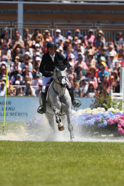 Cavallo grigio con cavaliere che attraversano l'acqua durante il Derby del Jumping de la Baule